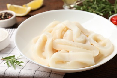 Photo of Uncooked squid rings and spices on wooden table, closeup