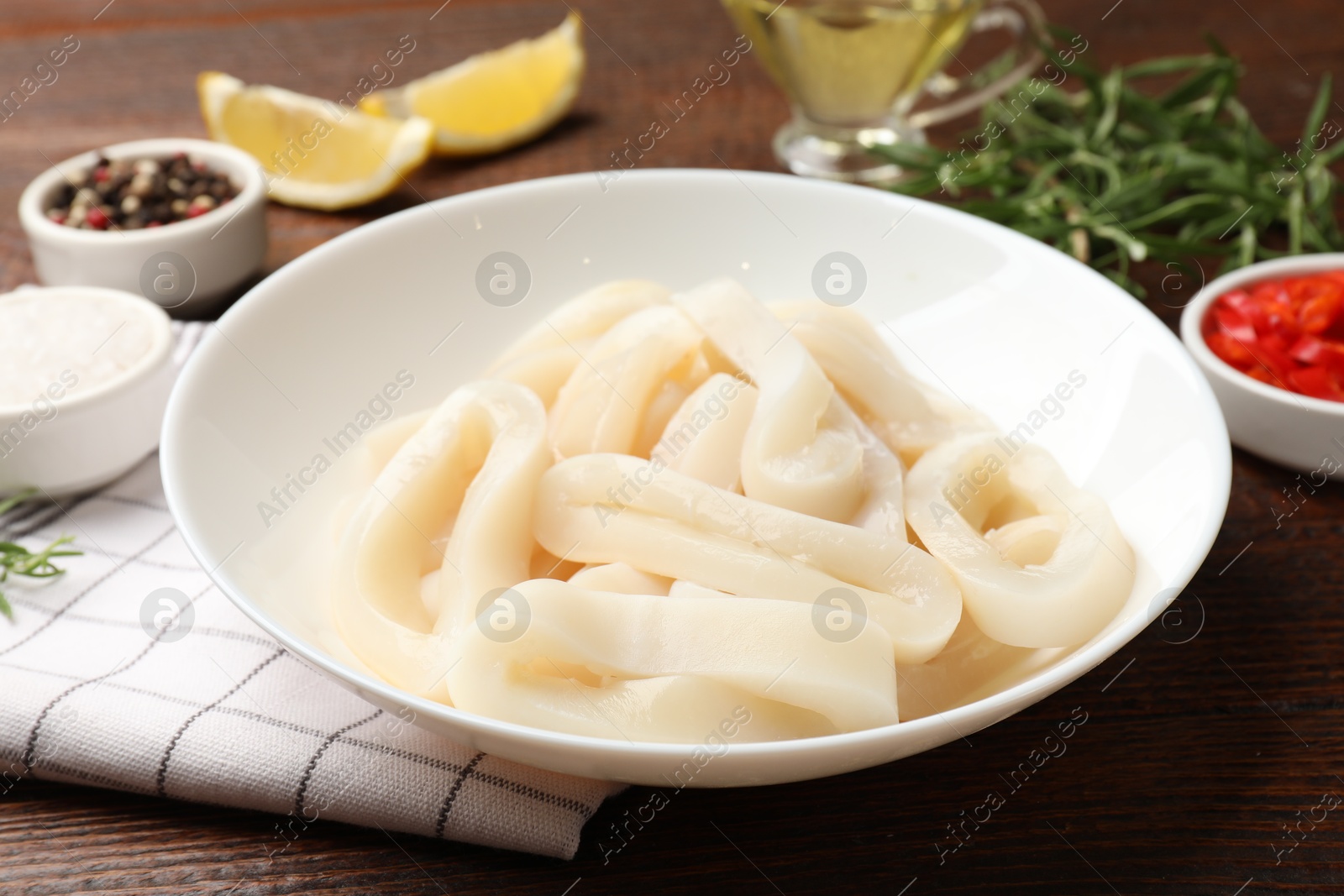 Photo of Uncooked squid rings and spices on wooden table, closeup