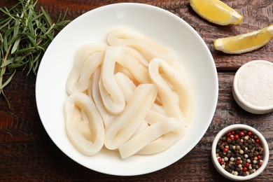 Photo of Uncooked squid rings and spices on wooden table, flat lay