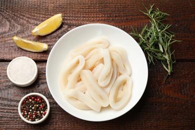 Photo of Uncooked squid rings and spices on wooden table, flat lay