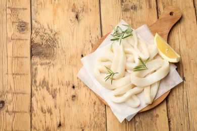 Photo of Uncooked squid rings with lemon slice and rosemary on wooden table, top view. Space for text