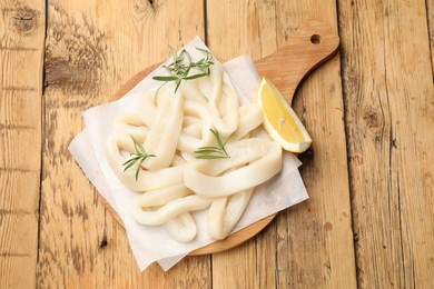 Photo of Uncooked squid rings with lemon slice and rosemary on wooden table, top view