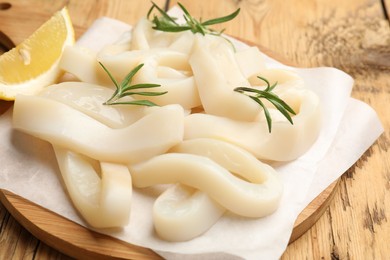 Photo of Uncooked squid rings with lemon slice and rosemary on wooden table, closeup