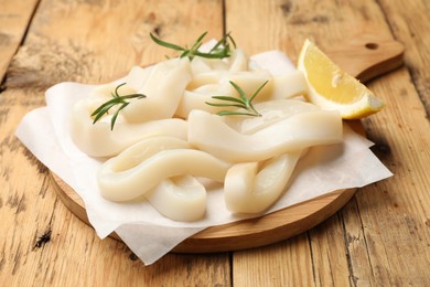 Photo of Uncooked squid rings with lemon slice and rosemary on wooden table, closeup