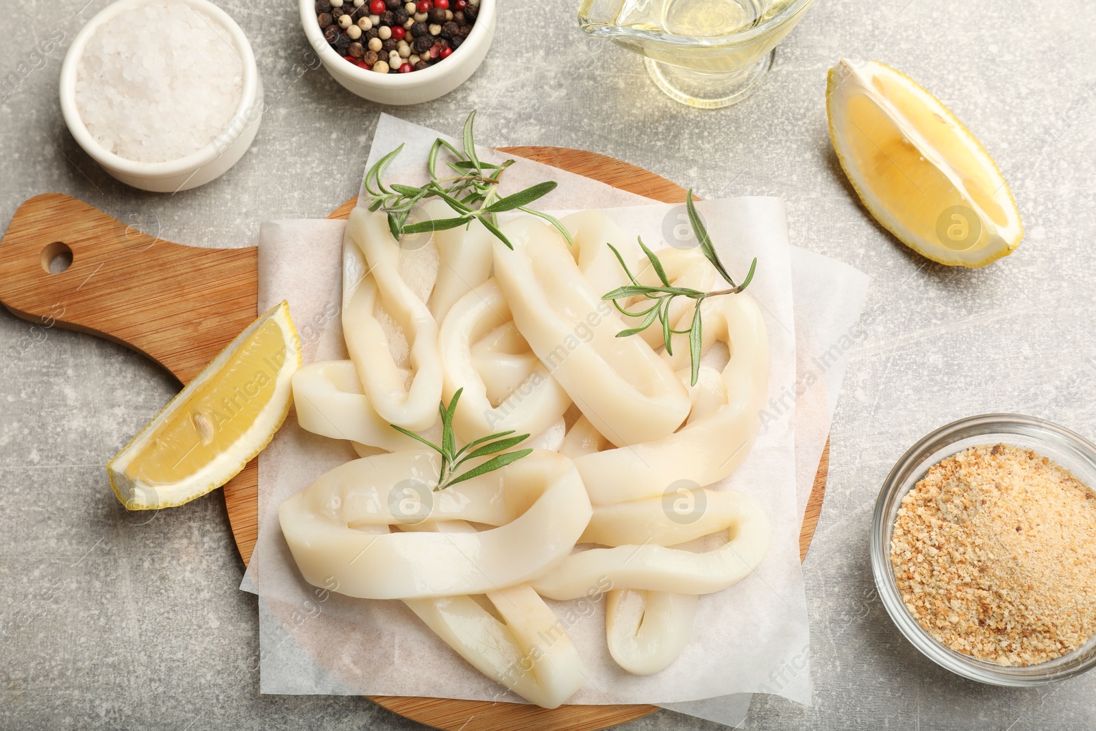 Photo of Uncooked squid rings, spices and bread crumbs on grey table, flat lay