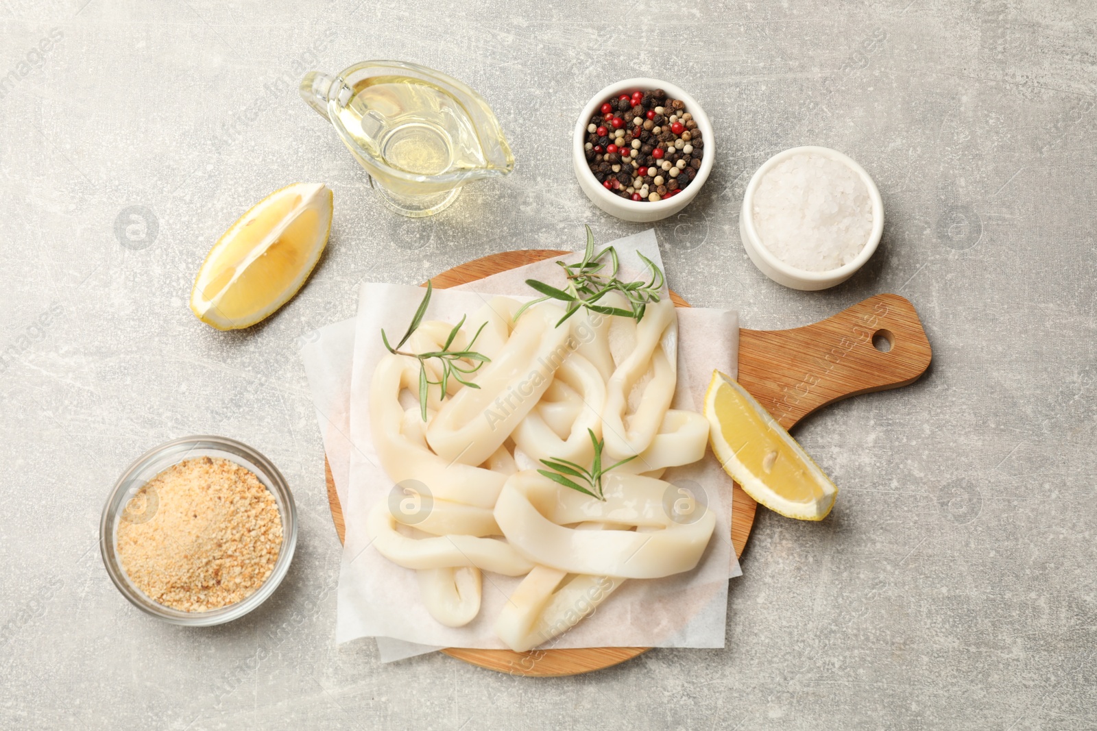 Photo of Uncooked squid rings, spices and bread crumbs on grey table, flat lay
