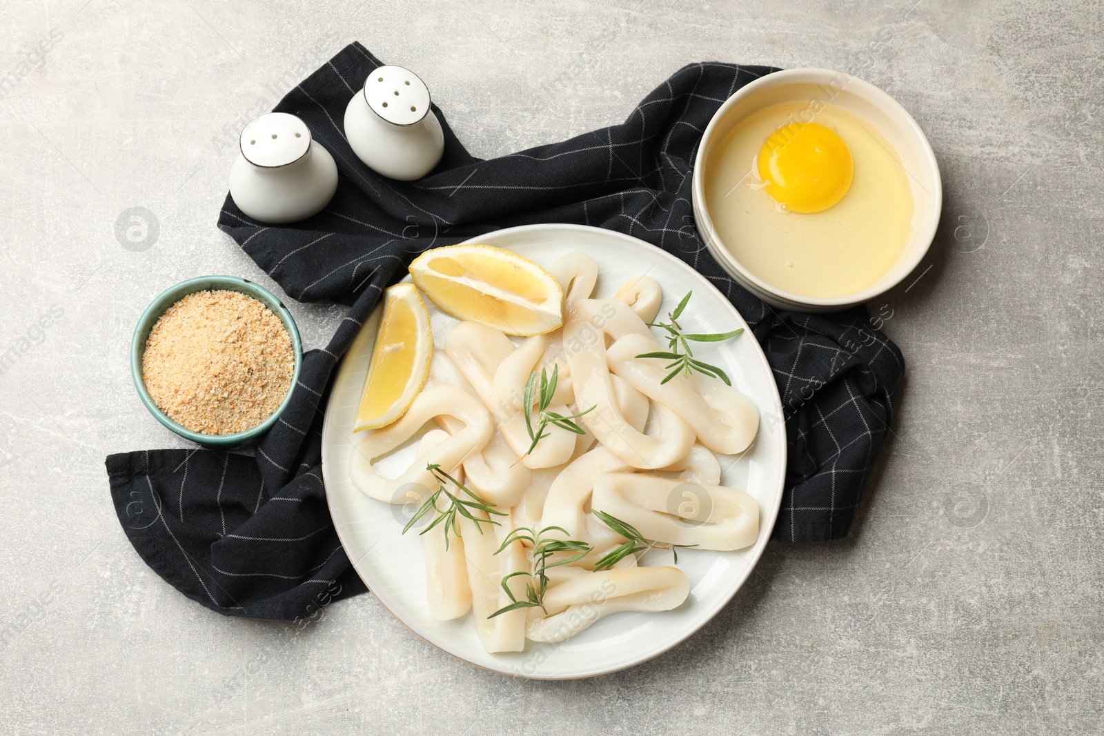 Photo of Uncooked squid rings and ingredients on grey table, flat lay