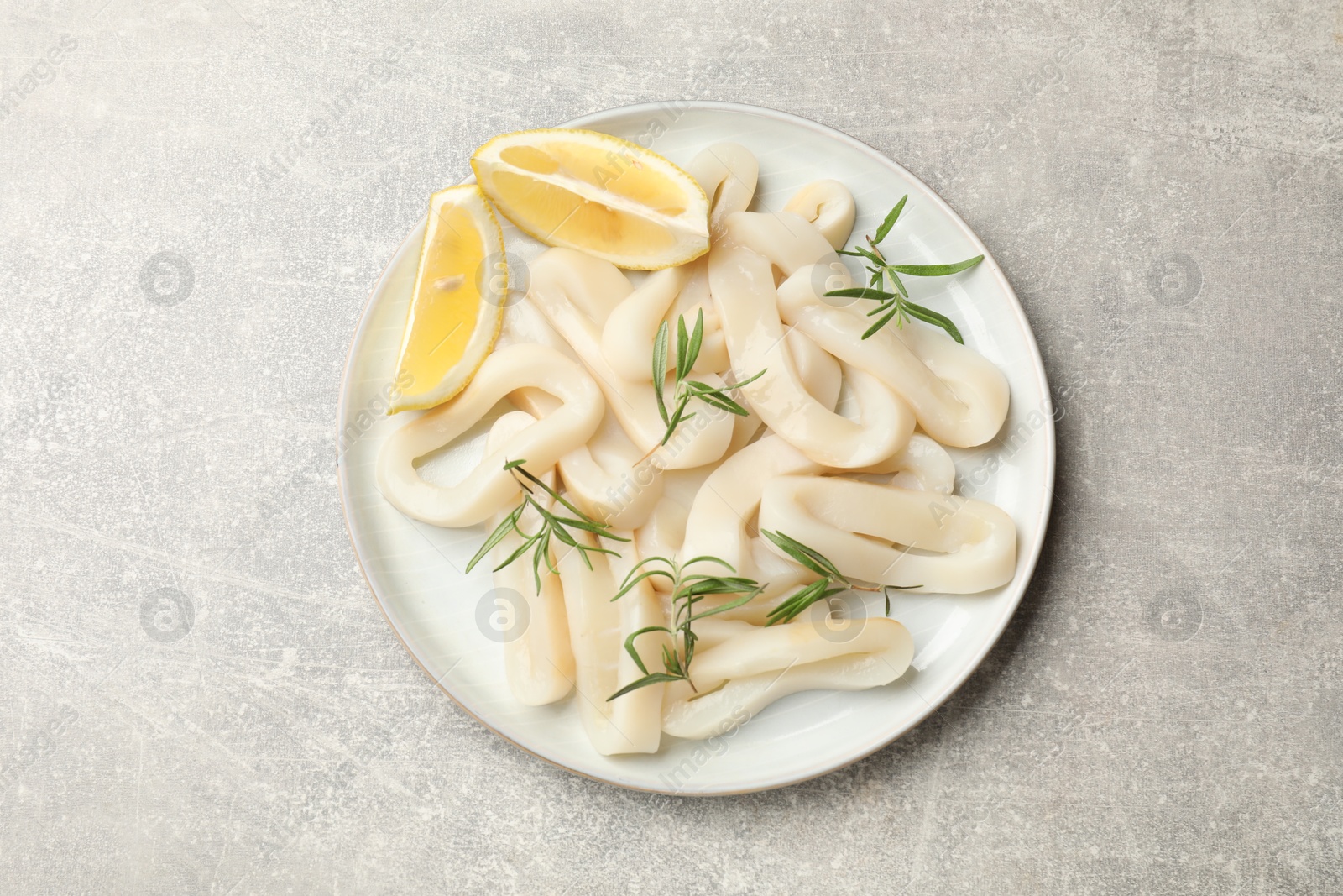 Photo of Uncooked squid rings with lemon slices and rosemary on grey table, top view