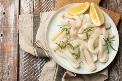 Photo of Uncooked squid rings with lemon slices and rosemary on wooden table, top view. Space for text
