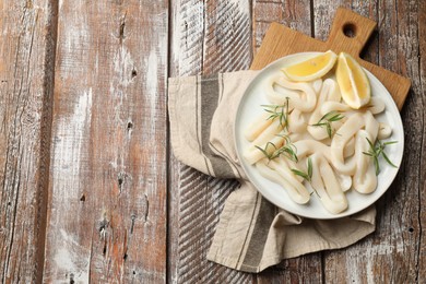 Photo of Uncooked squid rings with lemon slices and rosemary on wooden table, top view. Space for text