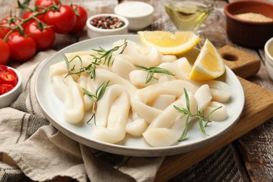 Photo of Uncooked squid rings, spices, tomatoes and bread crumbs on wooden table, closeup