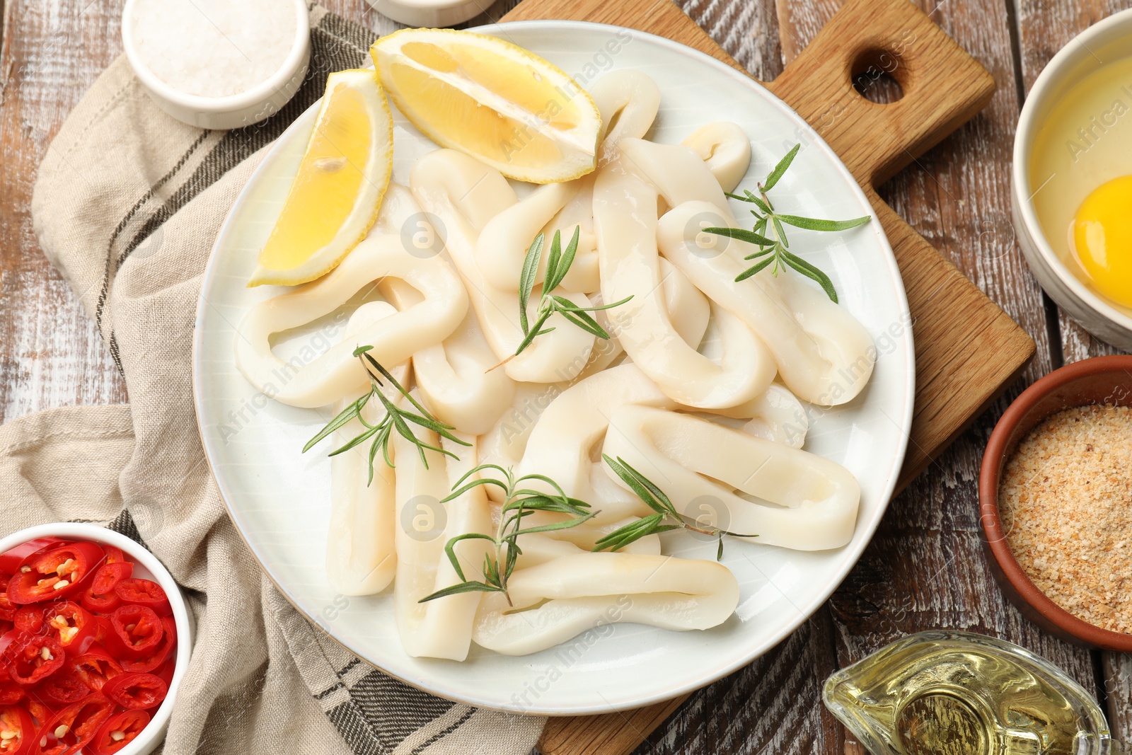 Photo of Uncooked squid rings, spices, yolk and bread crumbs on wooden table, flat lay