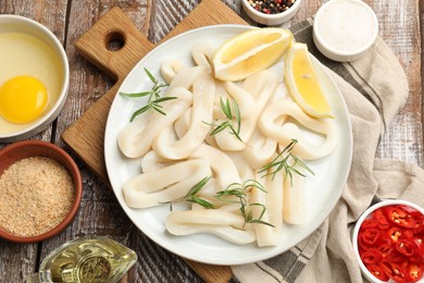 Photo of Uncooked squid rings, spices, yolk and bread crumbs on wooden table, flat lay