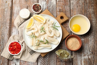 Photo of Uncooked squid rings, spices, yolk and bread crumbs on wooden table, flat lay