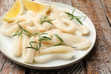 Photo of Uncooked squid rings with lemon slices and rosemary on wooden table, closeup