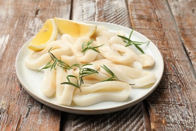Photo of Uncooked squid rings with lemon slices and rosemary on wooden table, closeup