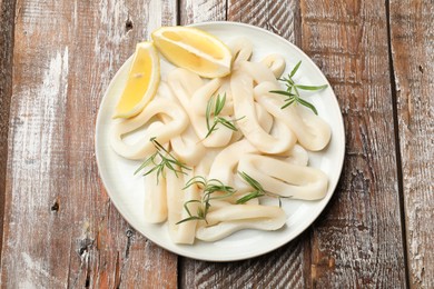 Photo of Uncooked squid rings with lemon slices and rosemary on wooden table, top view