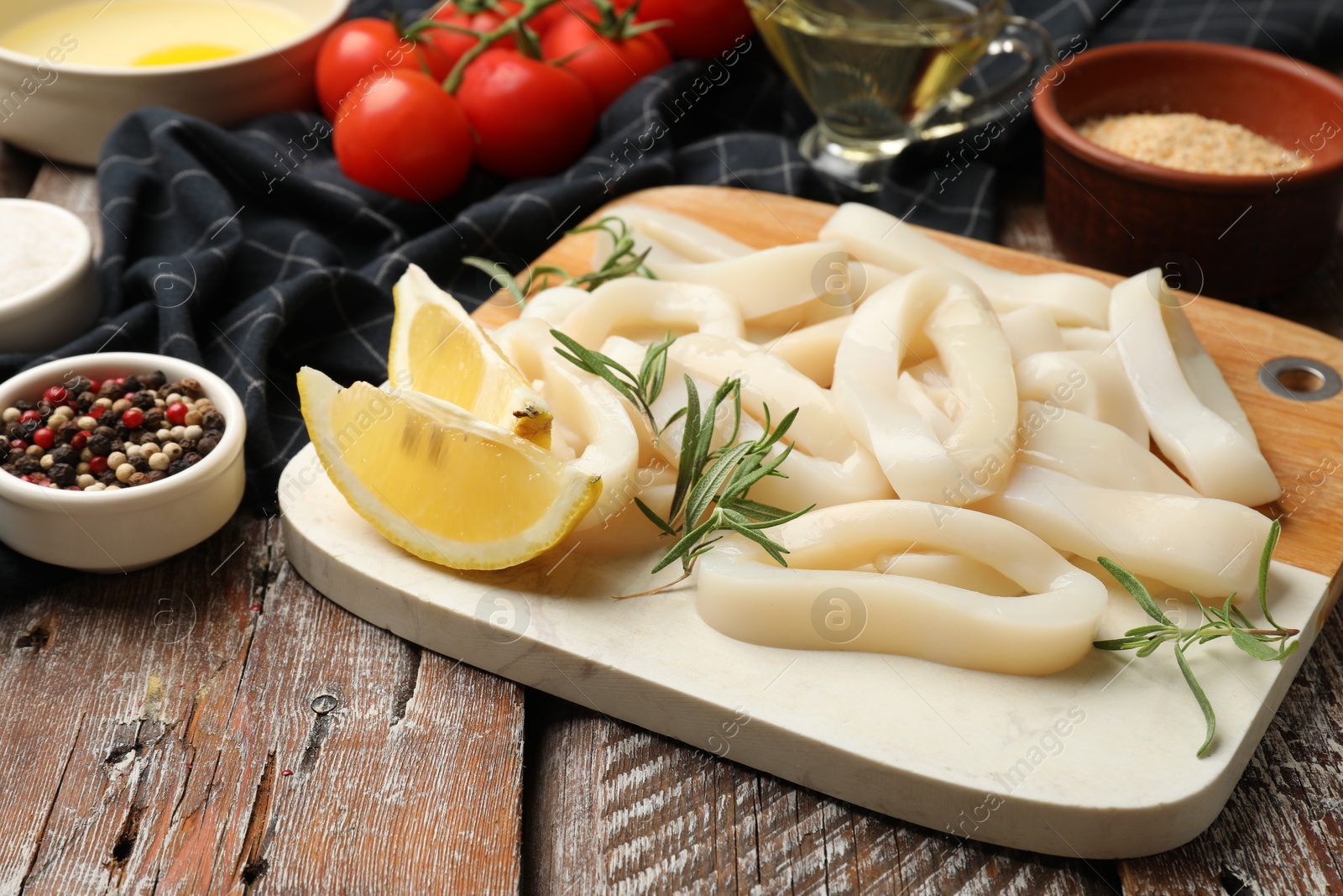Photo of Uncooked squid rings, spices, yolk, tomatoes and bread crumbs on wooden table, closeup
