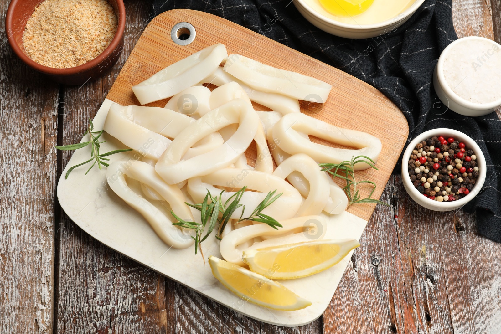 Photo of Uncooked squid rings, spices, yolk and bread crumbs on wooden table, flat lay