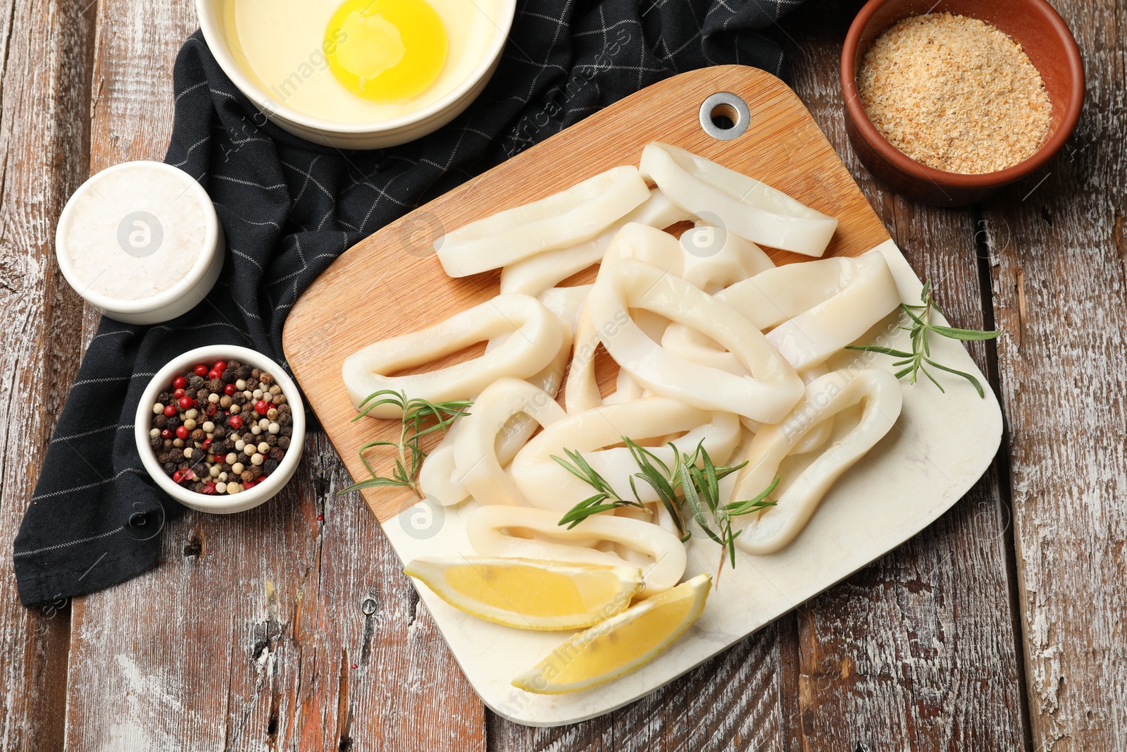 Photo of Uncooked squid rings, spices, yolk and bread crumbs on wooden table, flat lay