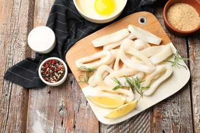 Photo of Uncooked squid rings, spices, yolk and bread crumbs on wooden table, flat lay