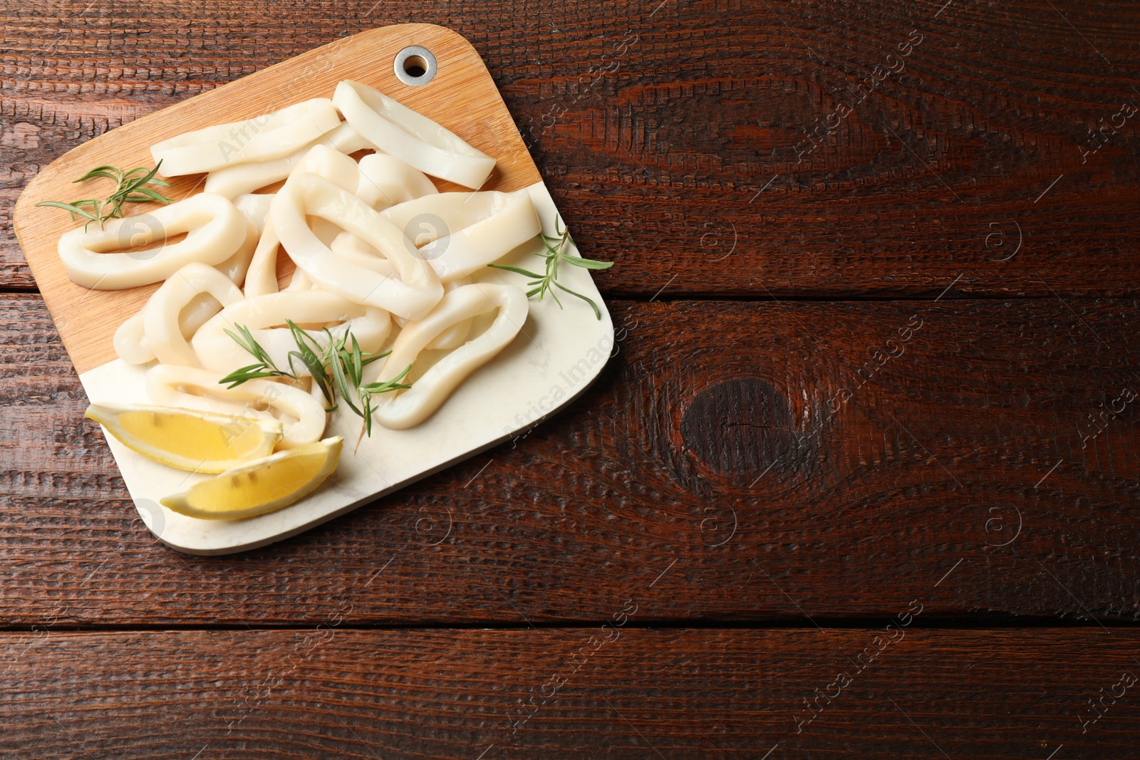 Photo of Uncooked squid rings with lemon slices and rosemary on wooden table, top view. Space for text