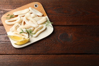 Photo of Uncooked squid rings with lemon slices and rosemary on wooden table, top view. Space for text