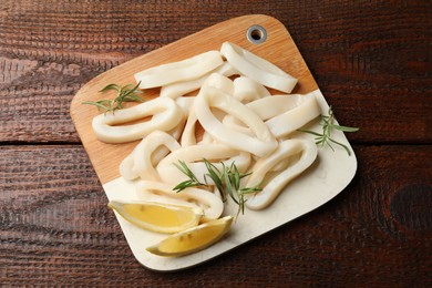 Photo of Uncooked squid rings with lemon slices and rosemary on wooden table, top view
