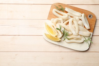 Photo of Uncooked squid rings with lemon slices and rosemary on wooden table, top view. Space for text