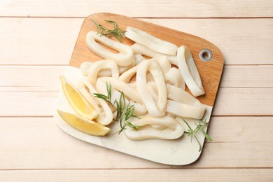 Photo of Uncooked squid rings with lemon slices and rosemary on wooden table, top view
