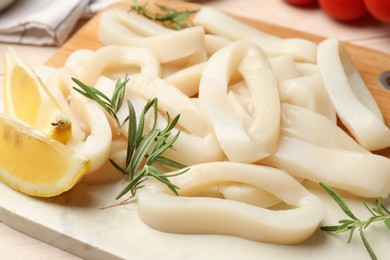 Photo of Uncooked squid rings with lemon slices and rosemary on table, closeup