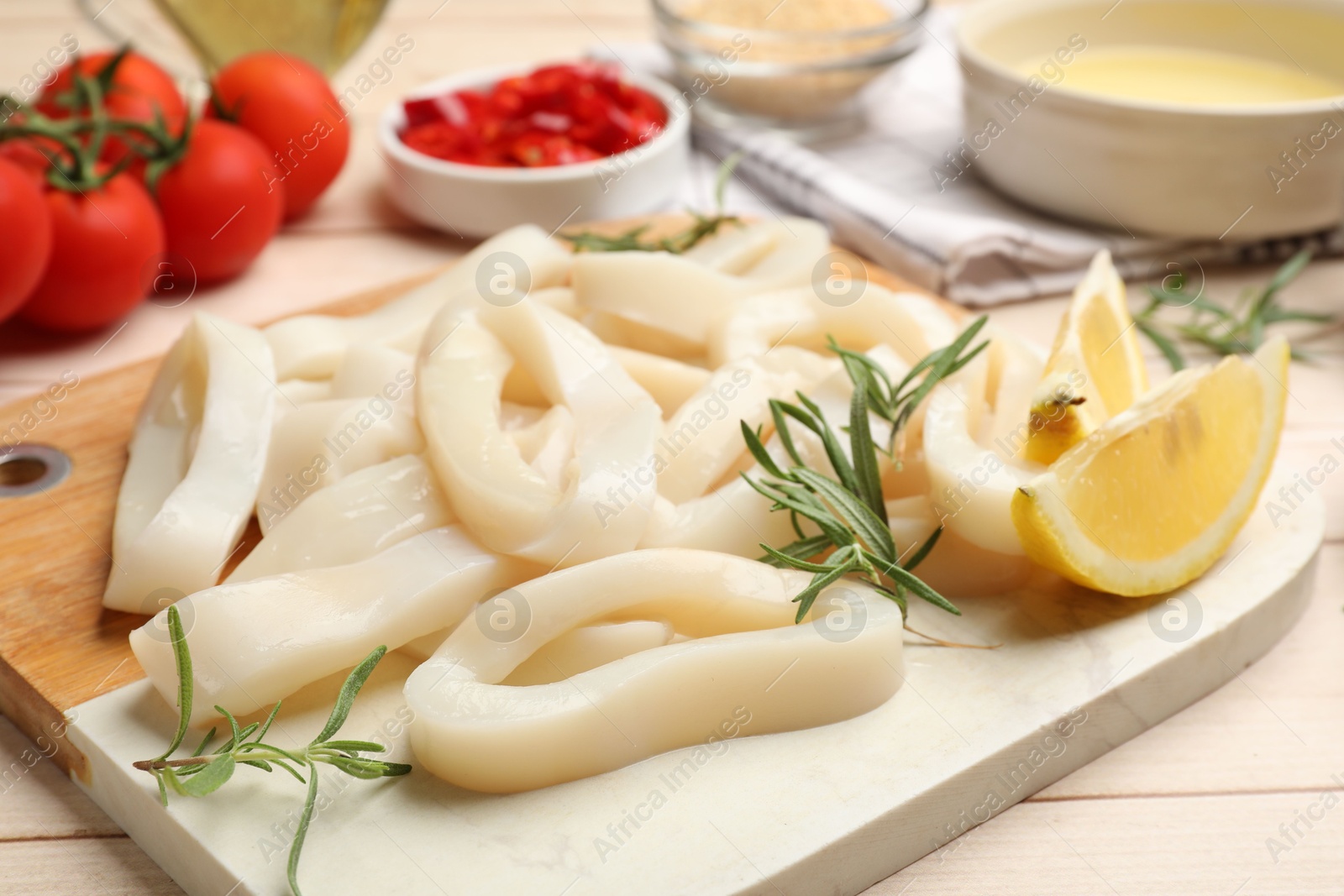 Photo of Uncooked squid rings, spices, yolk and tomatoes on wooden table, closeup