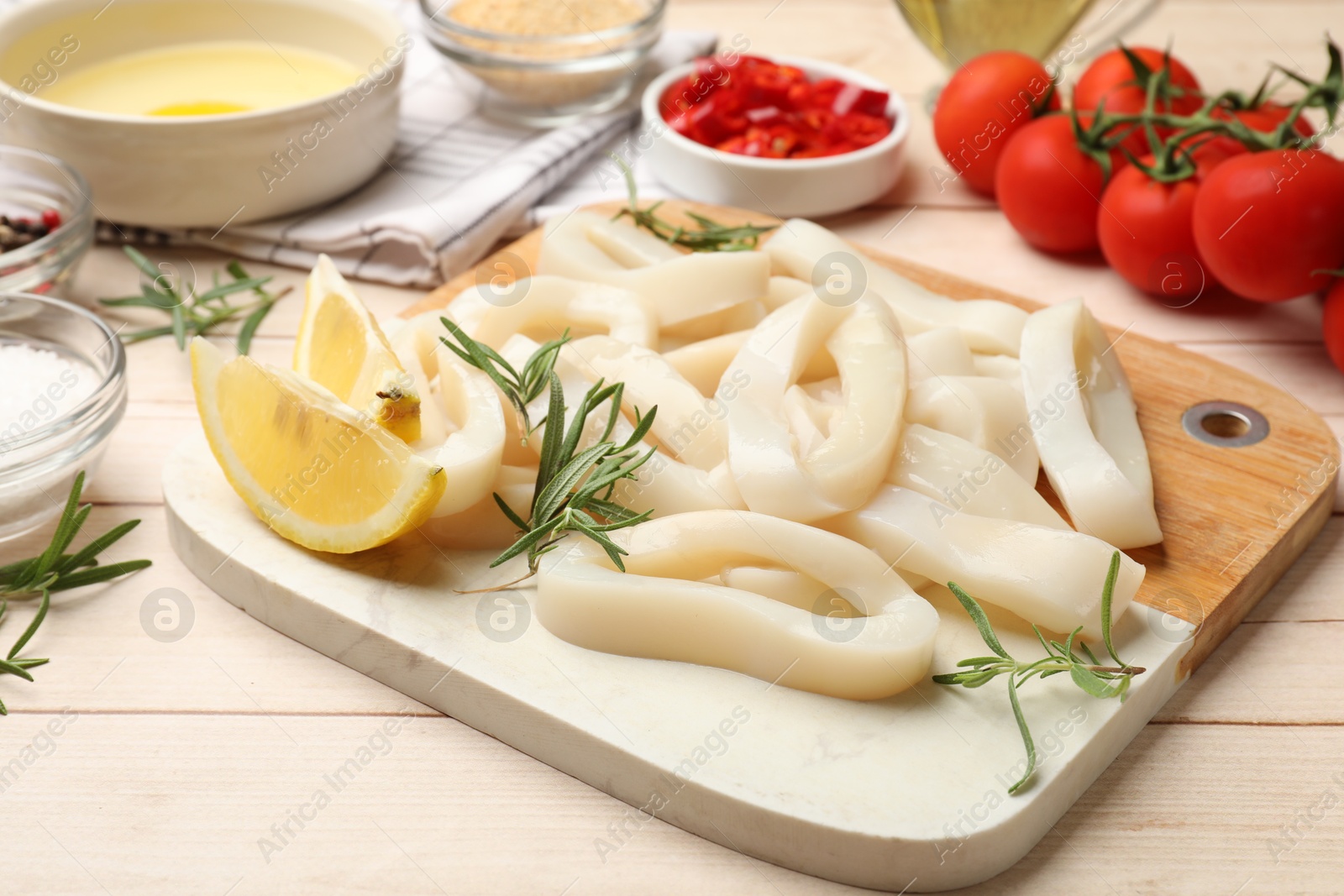 Photo of Uncooked squid rings, spices, yolk, tomatoes and bread crumbs on wooden table, closeup