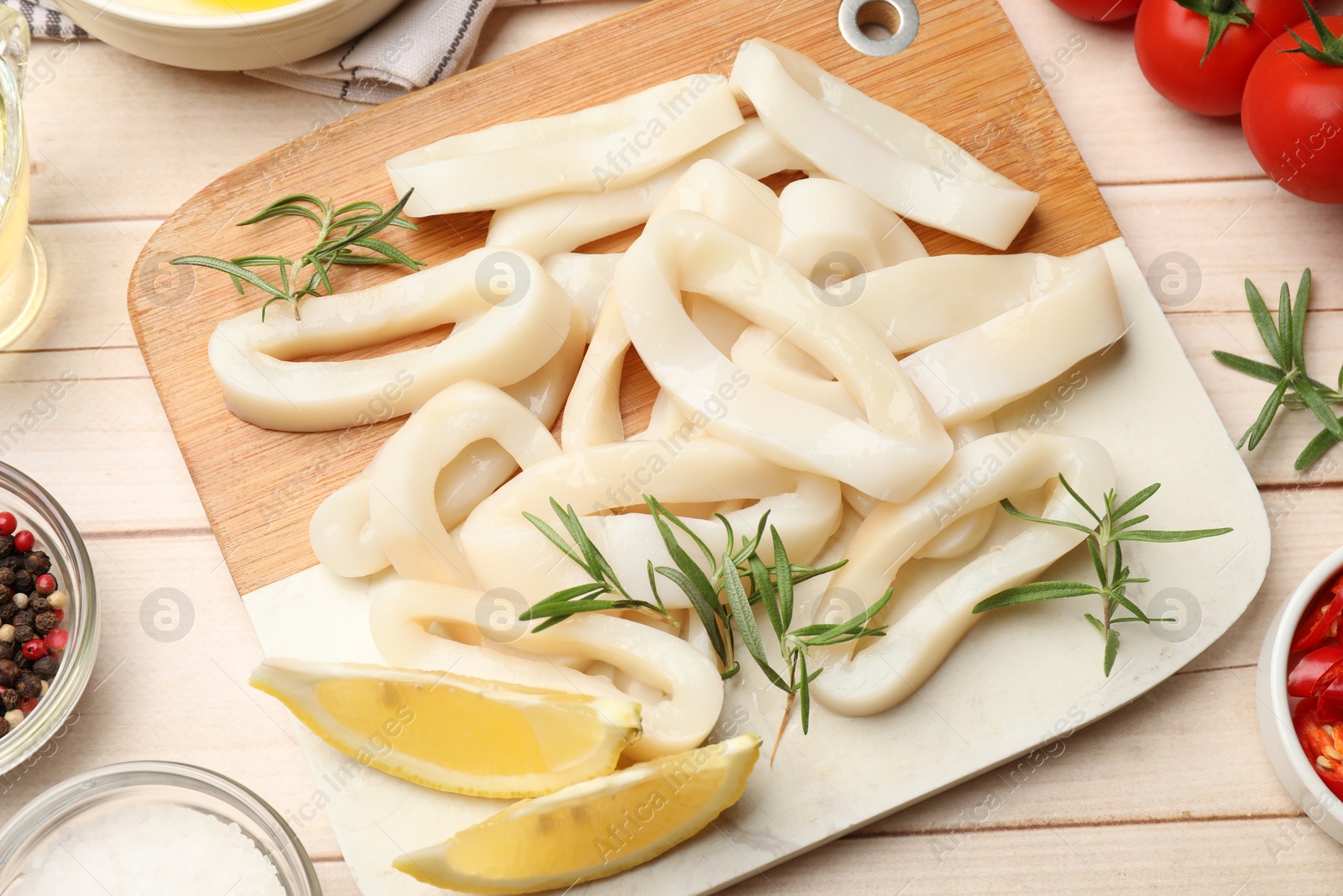 Photo of Uncooked squid rings, spices and tomatoes on wooden table, flat lay