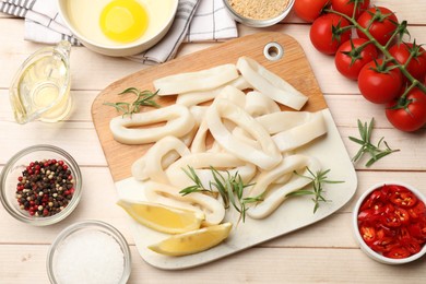 Photo of Uncooked squid rings, spices, yolk, bread crumbs and tomatoes on wooden table, flat lay