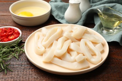 Photo of Uncooked squid rings, spices and yolk on wooden table, closeup