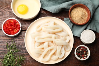 Photo of Uncooked squid rings, spices, yolk and bread crumbs on wooden table, flat lay