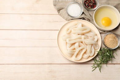 Photo of Uncooked squid rings, spices, yolk and bread crumbs on wooden table, flat lay. Space for text