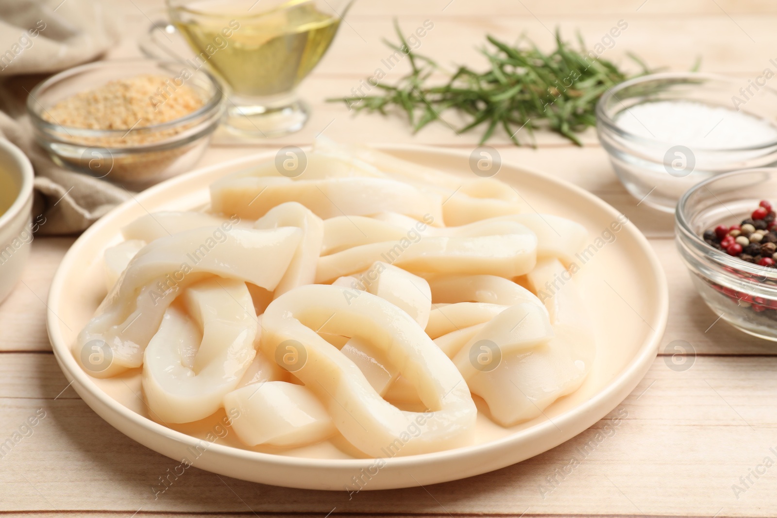 Photo of Uncooked squid rings, spices and bread crumbs on wooden table, closeup
