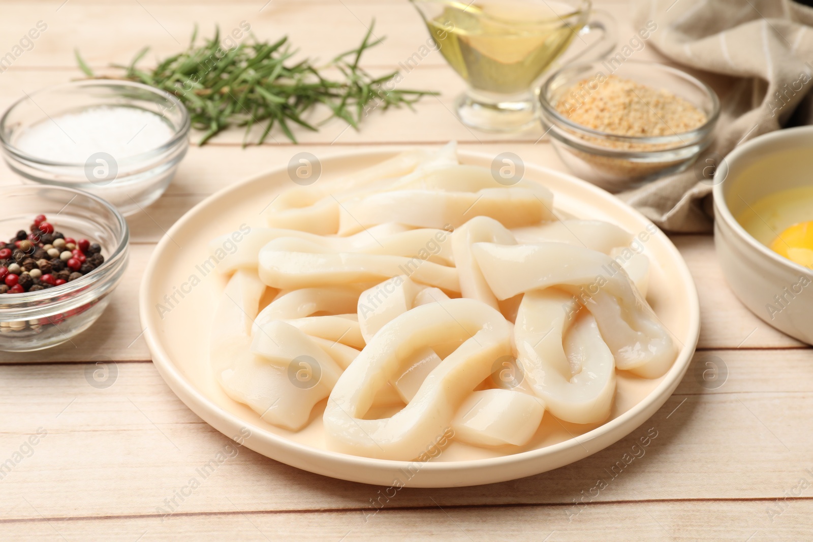 Photo of Uncooked squid rings, spices, yolk and bread crumbs on wooden table, closeup