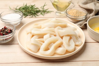 Photo of Uncooked squid rings, spices, yolk and bread crumbs on wooden table, closeup