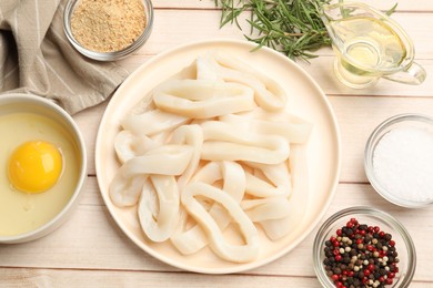 Photo of Uncooked squid rings, spices, yolk and bread crumbs on wooden table, flat lay