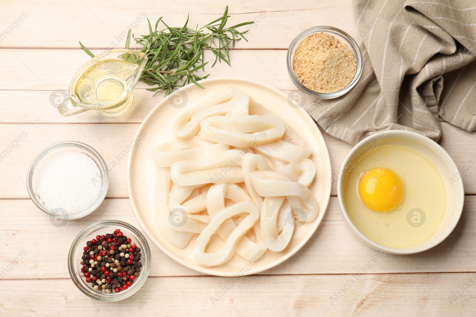 Photo of Uncooked squid rings, spices, yolk and bread crumbs on wooden table, flat lay