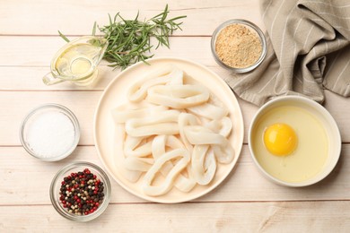 Photo of Uncooked squid rings, spices, yolk and bread crumbs on wooden table, flat lay