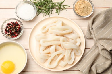 Photo of Uncooked squid rings, spices, yolk and bread crumbs on wooden table, flat lay