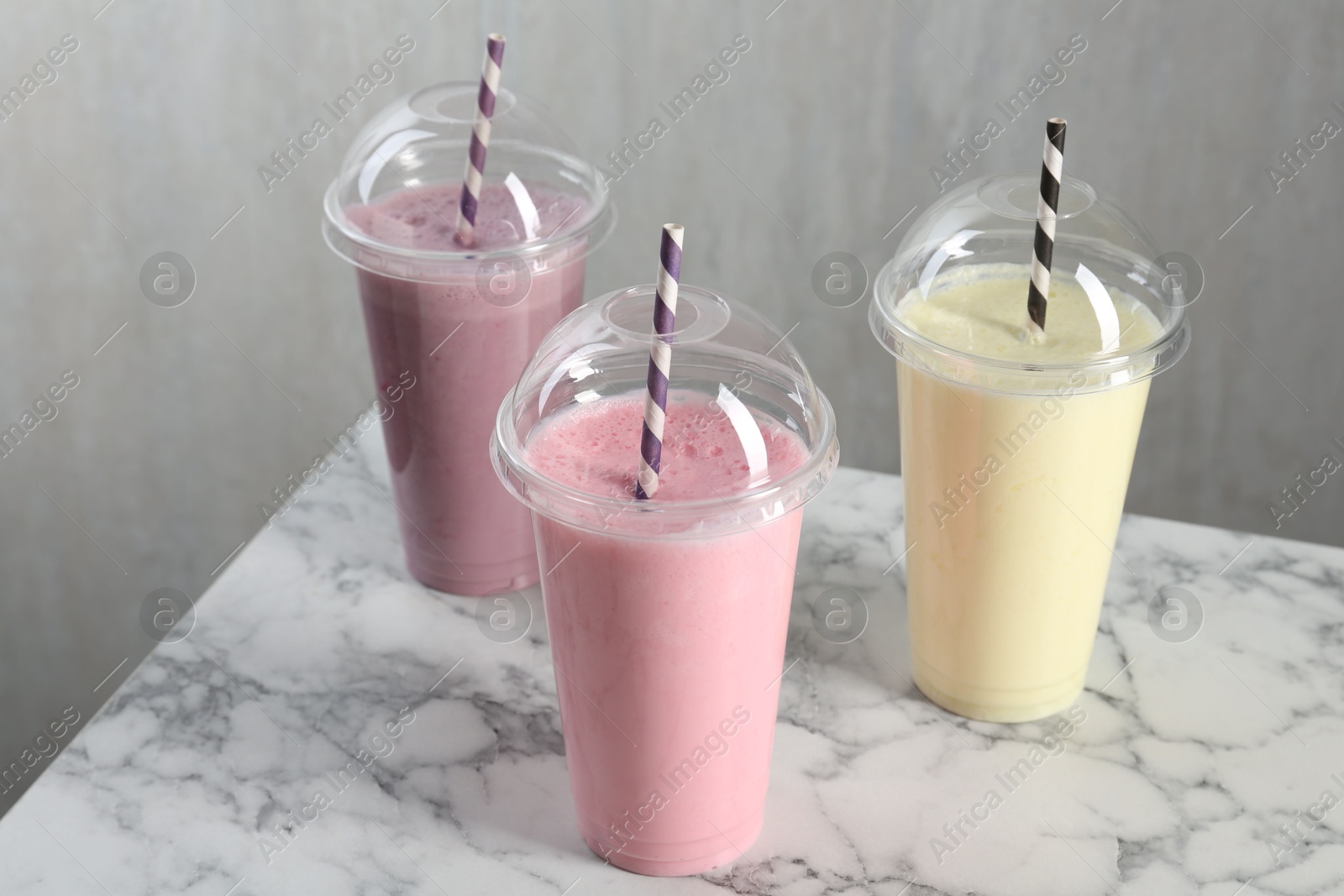 Photo of Milkshakes of different flavors in plastic cups on white marble table, closeup