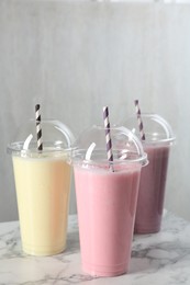 Photo of Milkshakes of different flavors in plastic cups on white marble table, closeup