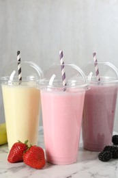Photo of Milkshakes of different flavors in plastic cups and ingredients on white marble table, closeup