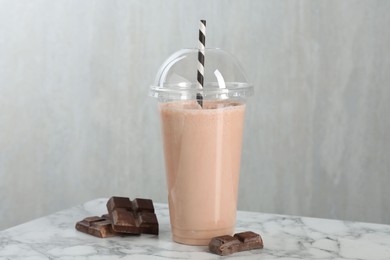 Photo of Tasty milkshake in plastic cup and chocolate pieces on white marble table, closeup