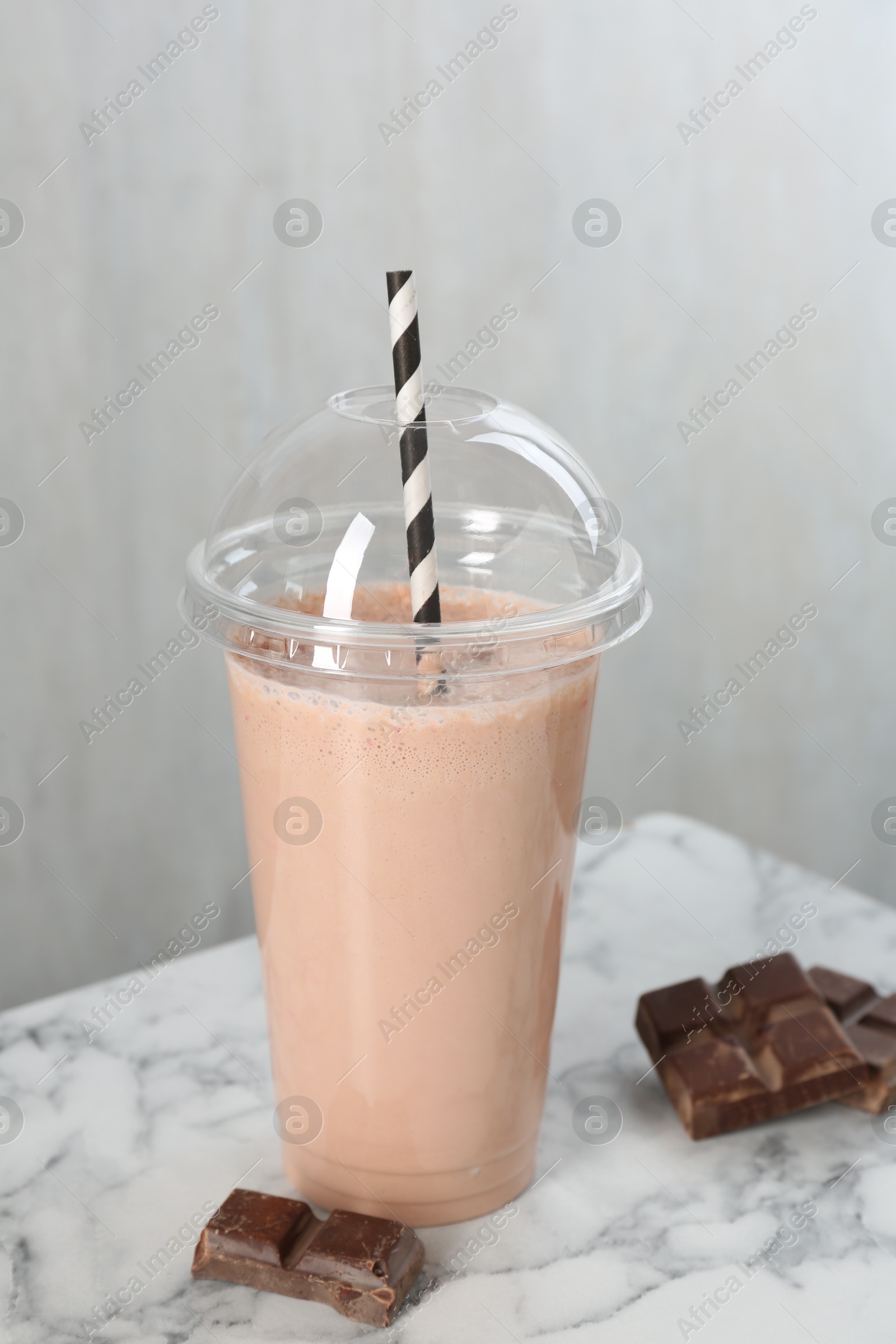 Photo of Tasty milkshake in plastic cup and chocolate pieces on white marble table